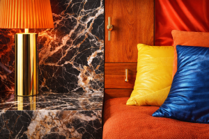 Détails d’un intérieur visuellement agressif mêlant surfaces brillantes, marbre très nervuré, bois orangé et textiles synthétiques aux couleurs saturées, illustrant des matières qui créent une tension visuelle.